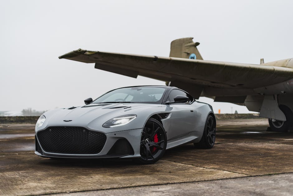 Sleek grey luxury car parked beneath an old aircraft on a foggy day